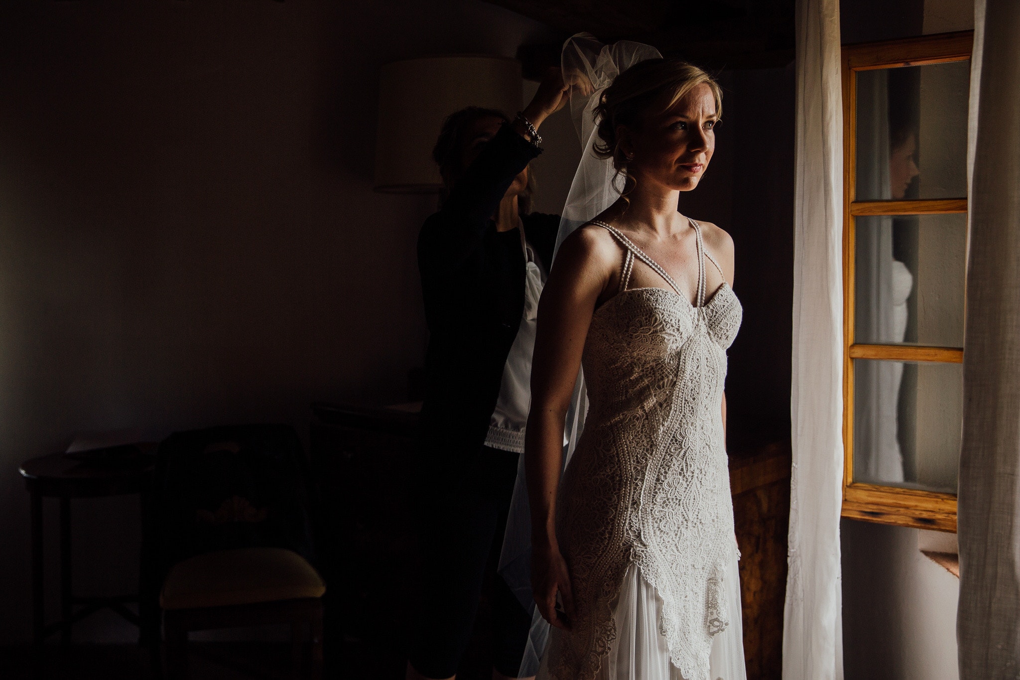 bride frame in window light putting veil on