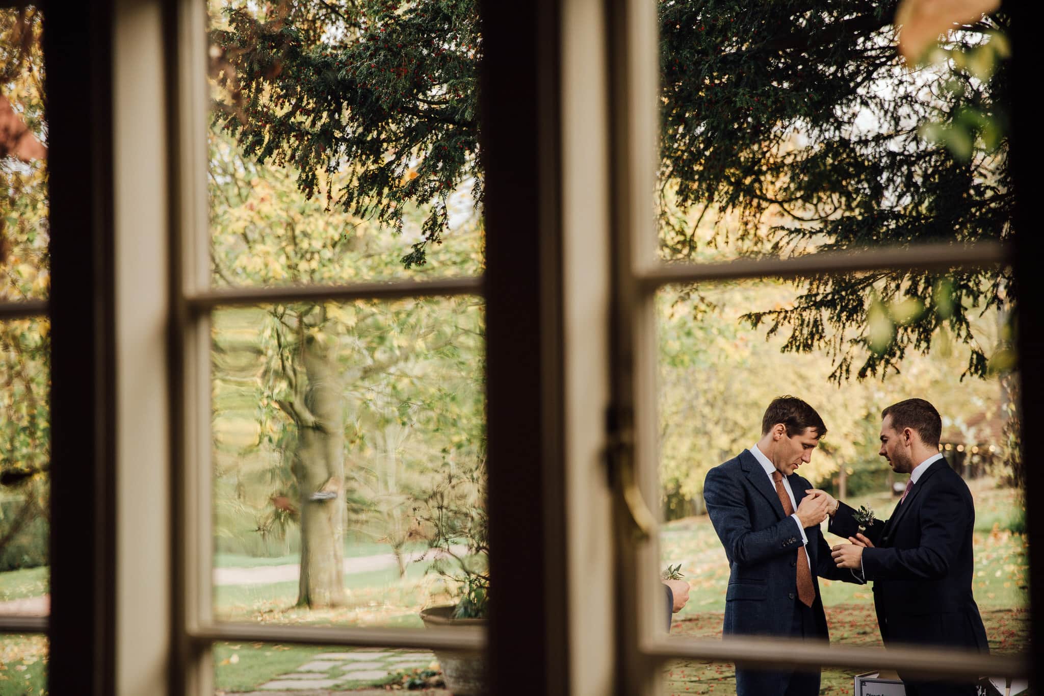 Groom framed in window putting on button hole