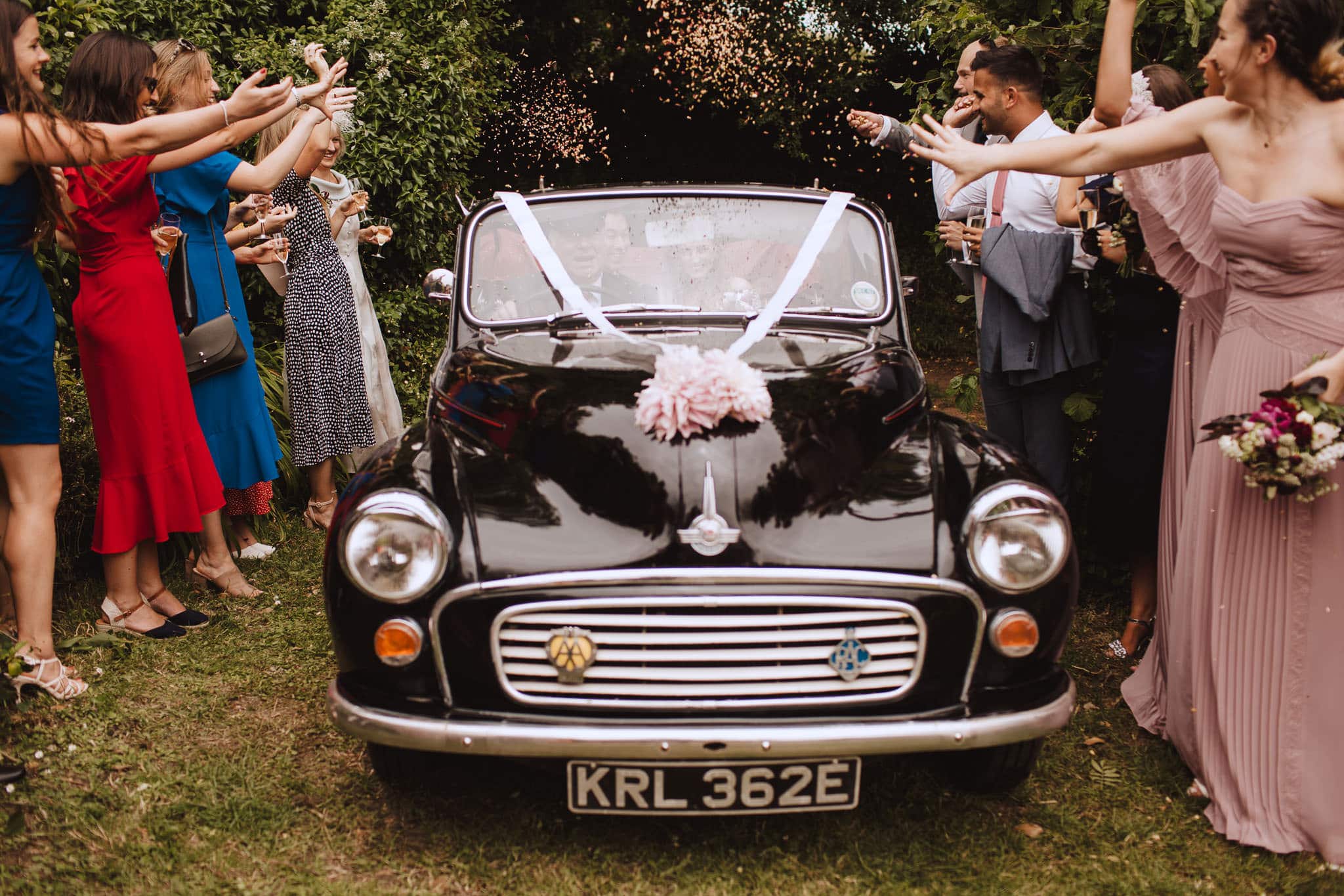 bride and groom drive through confetti tunnel in Morris Minor