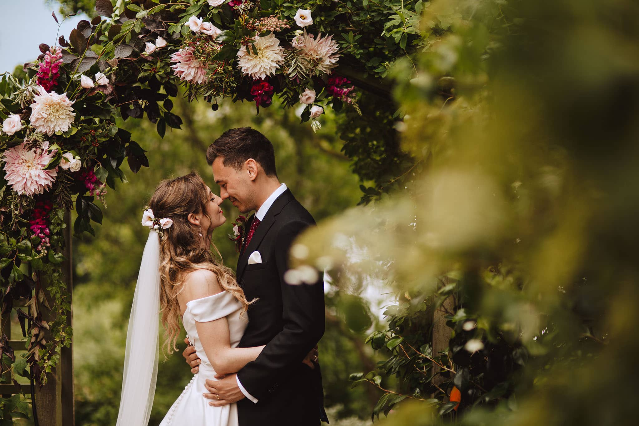 portrait of bride and groom under floral arch with dahlias at their Marquee Wedding at Home