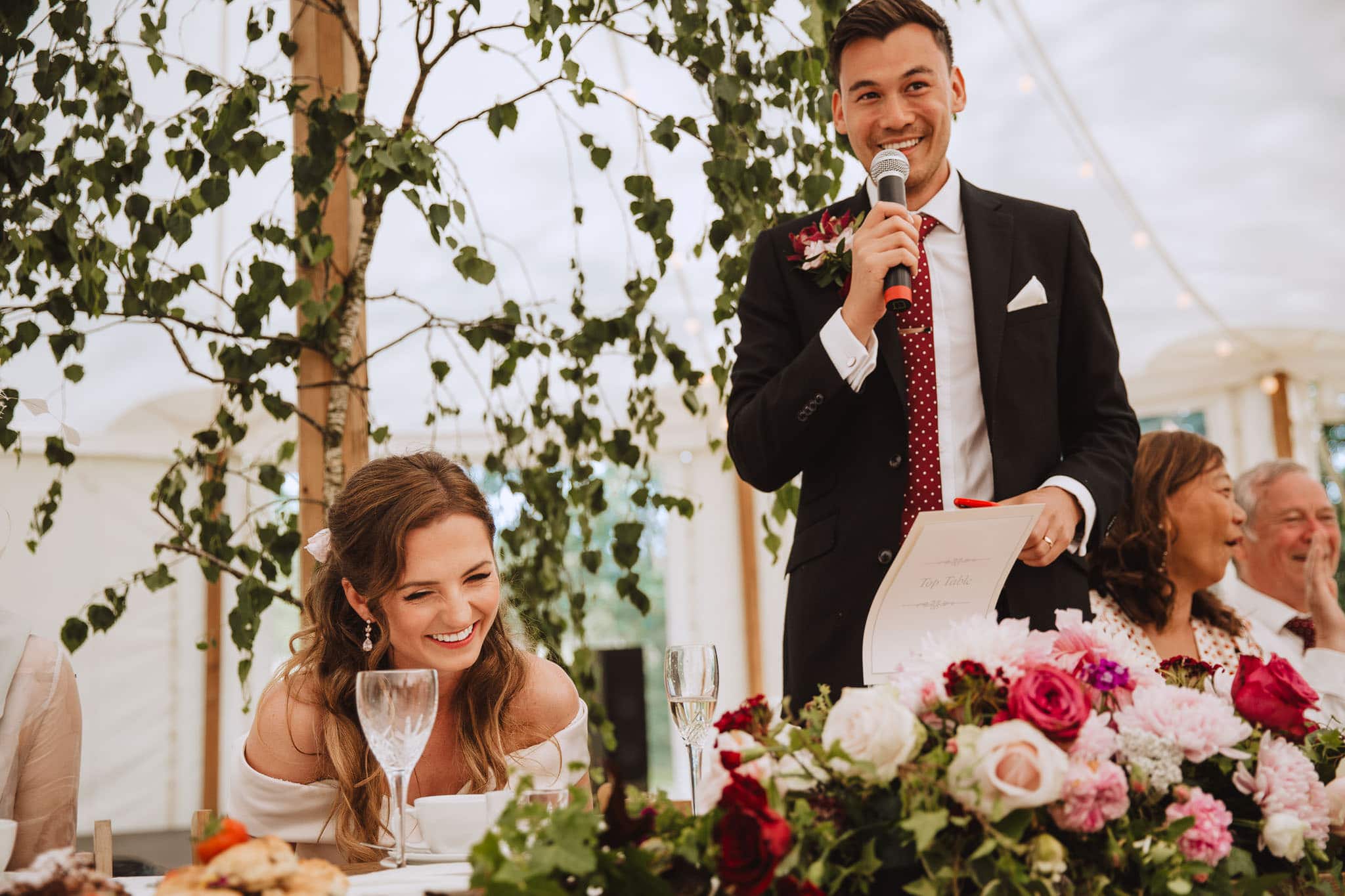 bride laughing at groom's speech in a marquee at their wedding at home