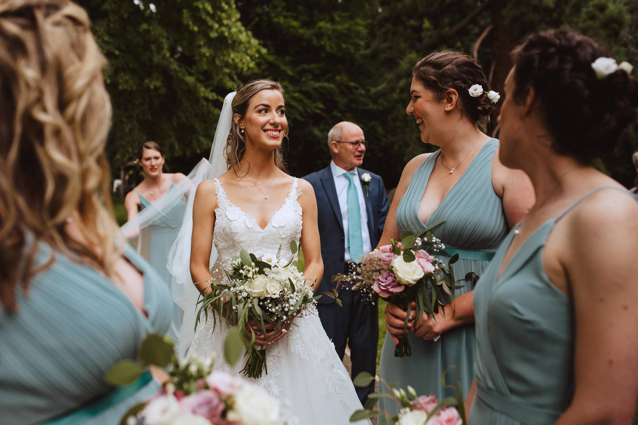 bride smiling eagerly with bridesmaids outside the Church in Leicestershire