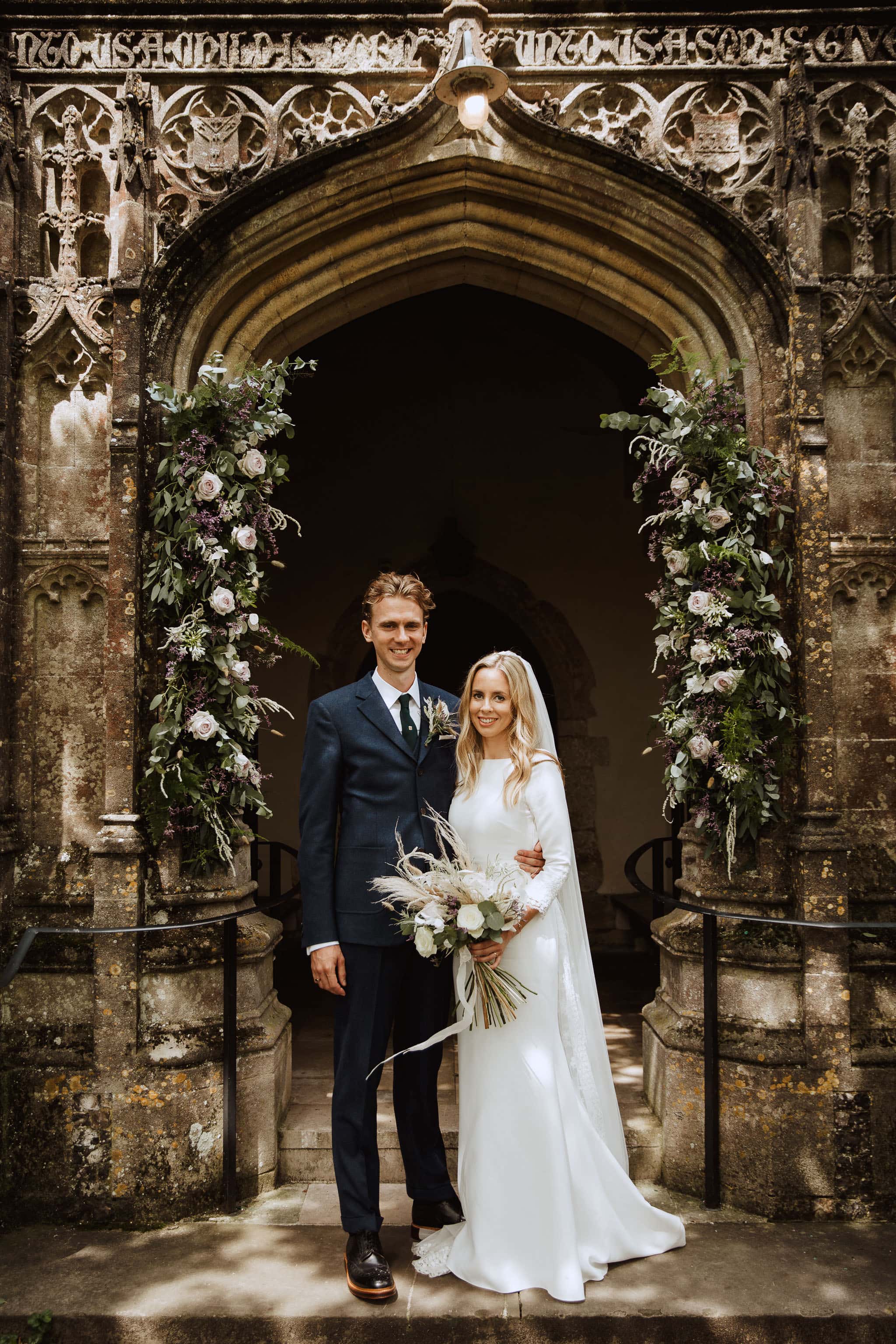 classic sophisticated Rime Arodaky Bride and groom in church doorway with beautiful flowers