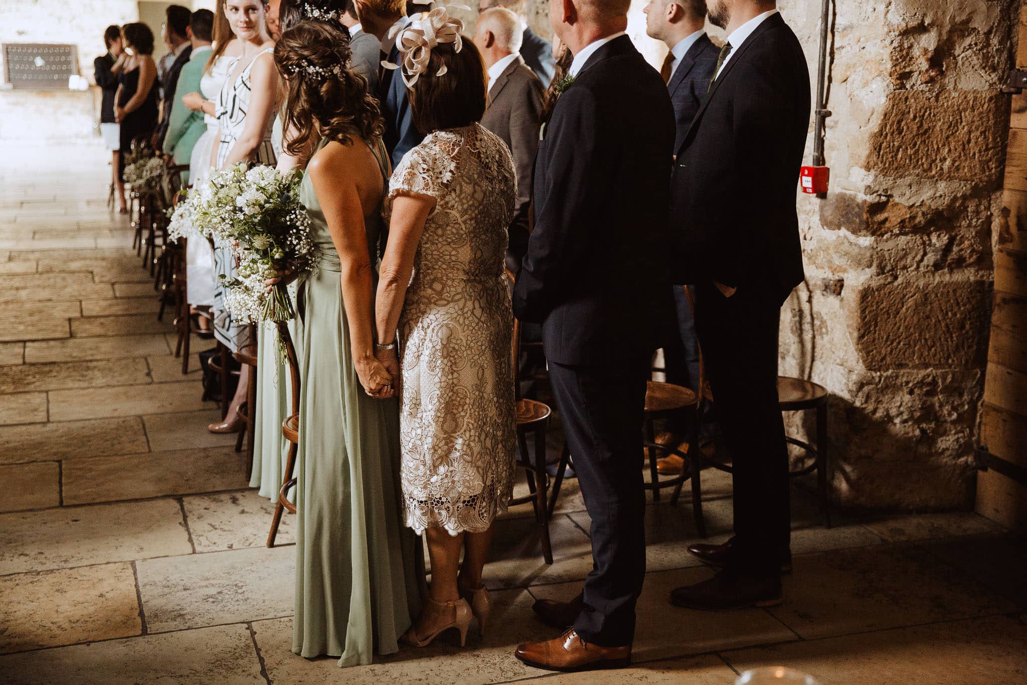 Mum and sister of the groom holding hands during the ceremony at Healey Barn