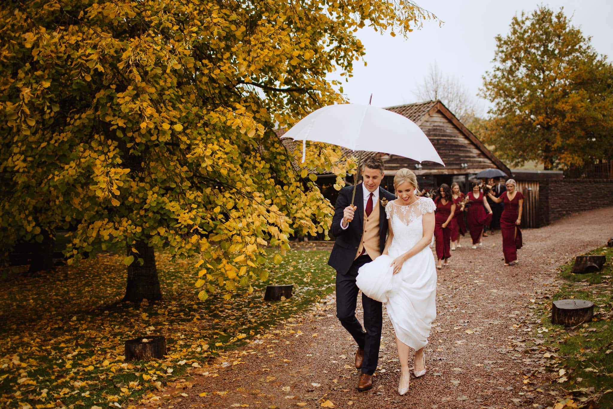Autumn Herefordshire wedding documentary shot of bride and groom leaving ceremony with umbrella