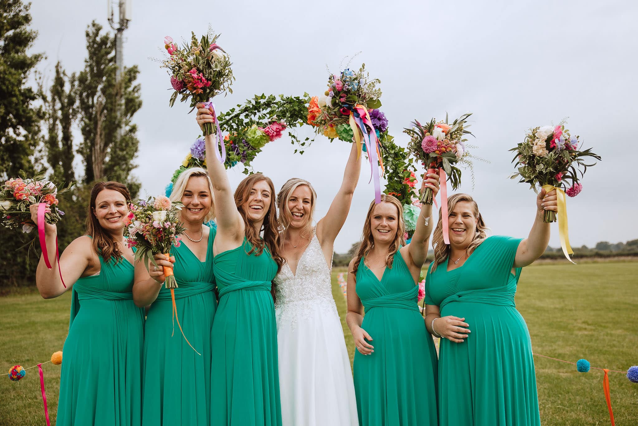 colourful DIY wedding with happy bride and bridesmaids cheering with bouquets in the air