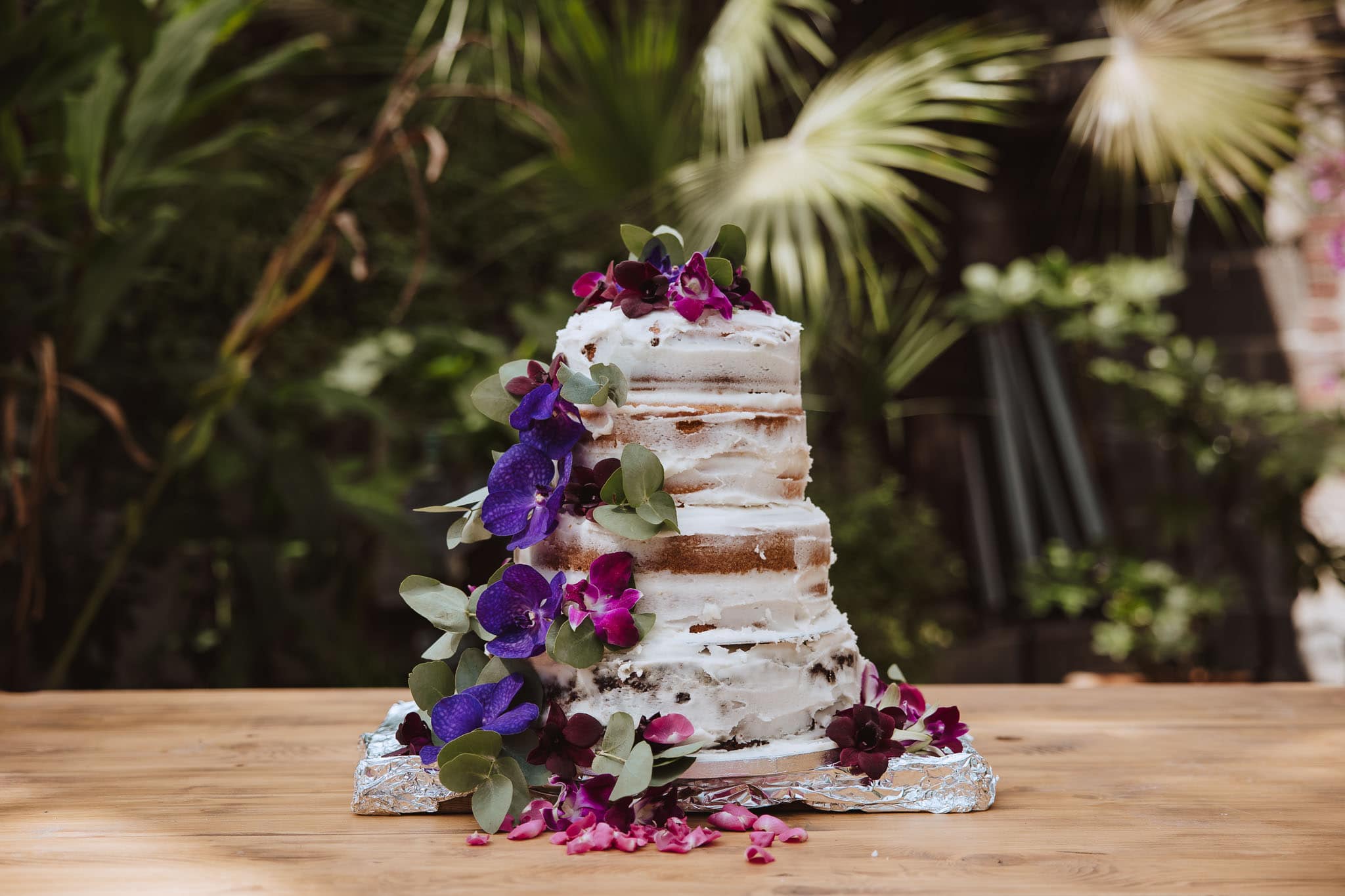 naked wedding cake with deep purple flowers