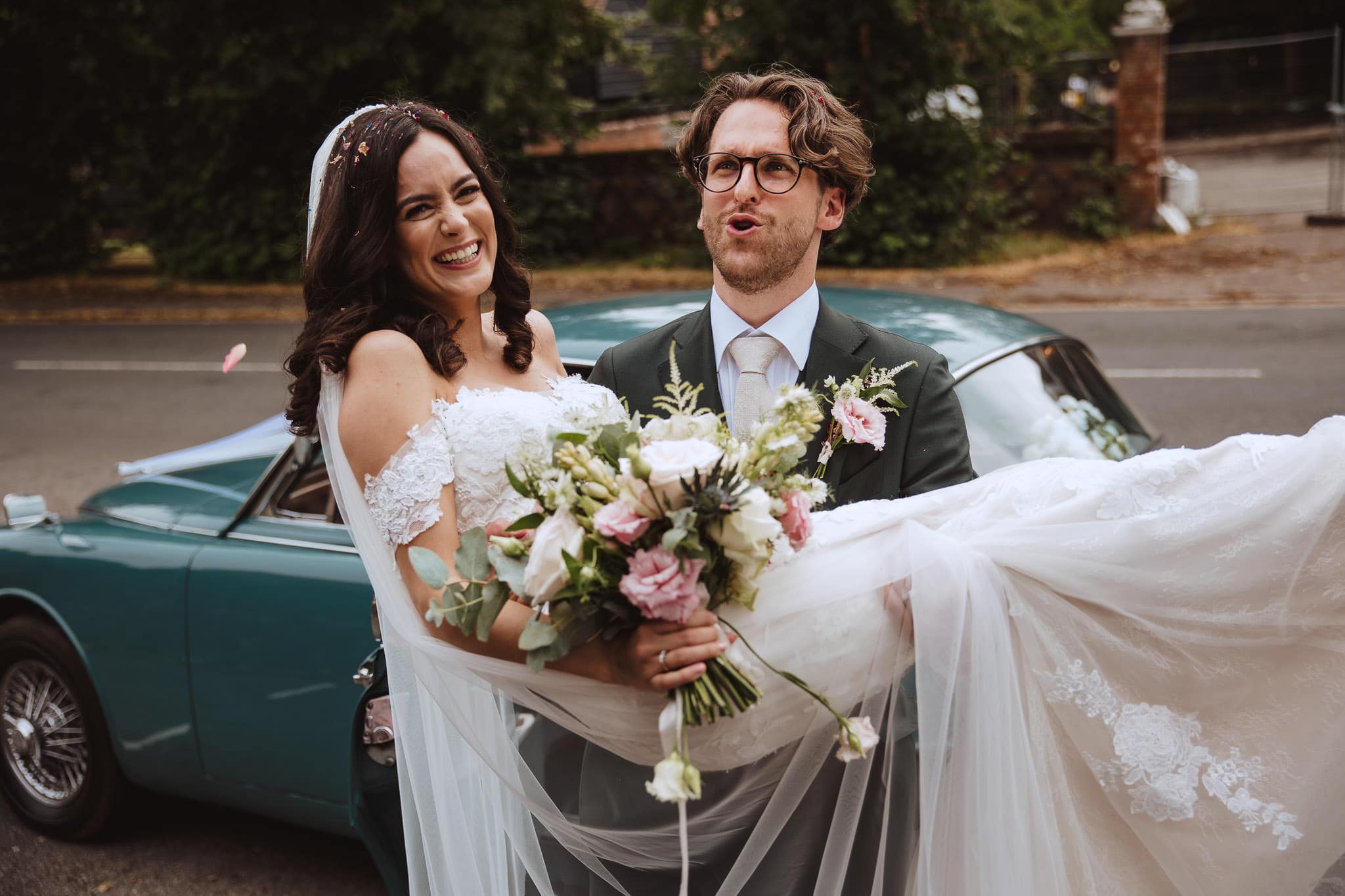 groom carrying his bride to their vintage wedding car